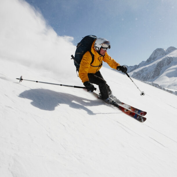 Eine skifahrende Person auf einer Piste vor Bergpanorama.