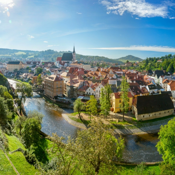 Mittelalterliche Kleinstadt mit Burg an einer Flussschlinge, umgeben von grünen Hügeln bei Sonnenschein.