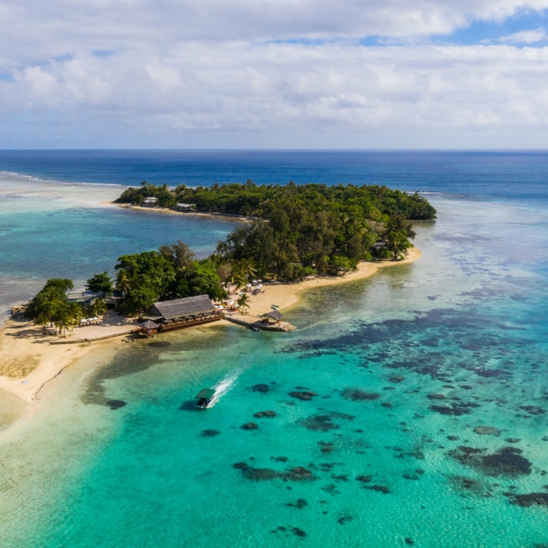 Kleine Insel mit Mangrovenwald und Bootsanleger an einem hellen Sandstrand, umgeben von türkisblauem Meer.