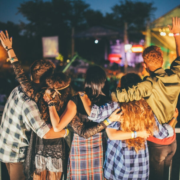 Jubelnde Zuschauer von hinten vor einer Bühne auf einem Musikfestival bei Nacht. 