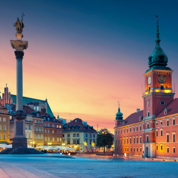 Beleuchteter Marktplatz in der Altstadt von Warschau mit Schlossbau aus rotem Stein und Siegessäule bei Abenddämmerung.