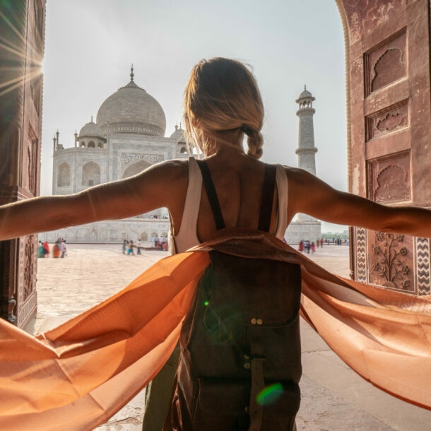 Rückansicht einer Frau mit Rucksack mit ausgestreckten Armen vor dem Taj Mahal.