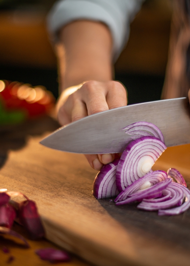 Person schneidet mit Küchenmesser eine rote Zwiebel