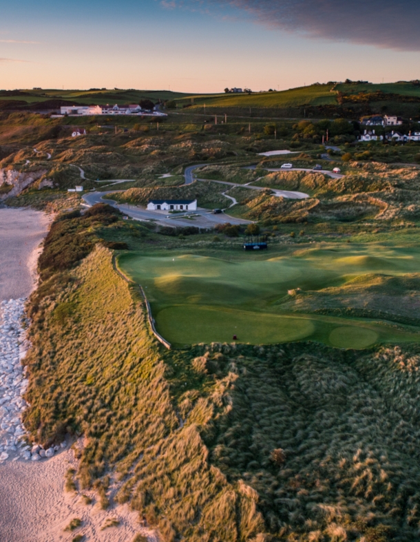 Blick auf einen Golfplatz und einen Küstenstreifen mit Sandstrand aus der Luft