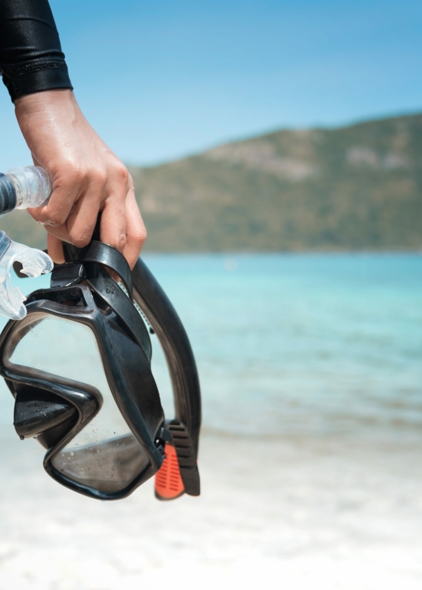 Eine Person am Strand hält eine Taucherbrille und einen Schnorchel