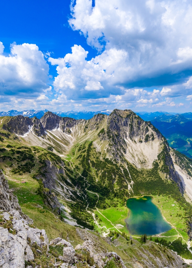 Luftaufnahme eines blaugrünen Bergsees unterhalb eines schroffen Gipfels