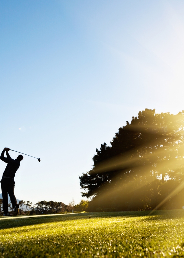 Die Silhouette eines ausholenden Golfspielers im Gegenlicht auf einem Golfplatz