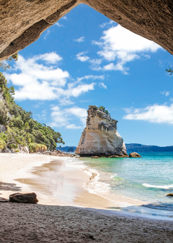 Im Vordergrund ein Felsbrocken, dahinter ein Sandstrand, umringt von Felsen und türkisfarbenem Meer