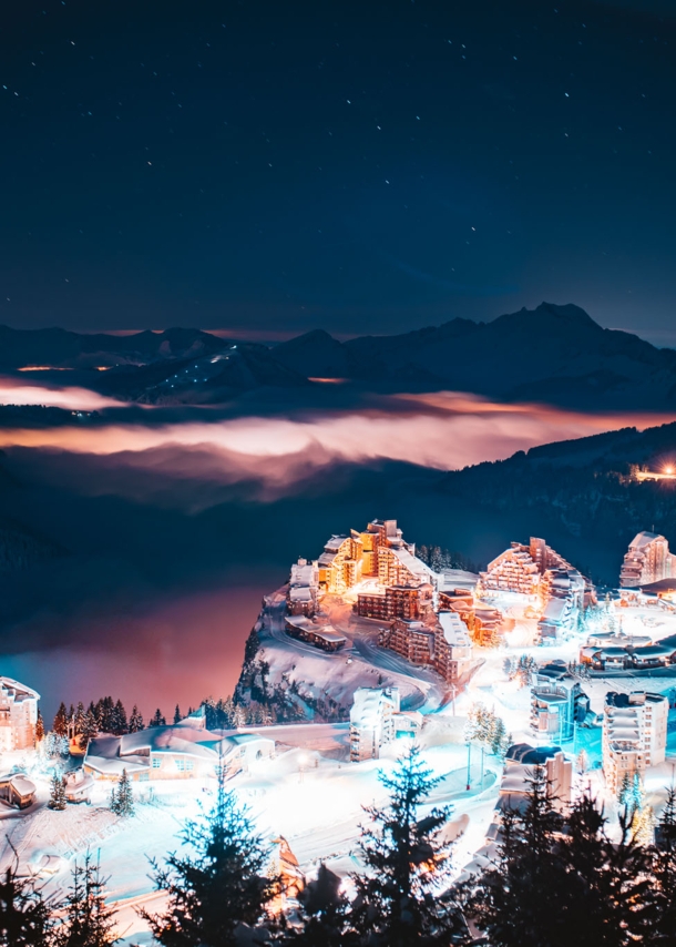 Eine erleuchtete Stadt bei Nacht, im Hintergrund dunkle Berge.