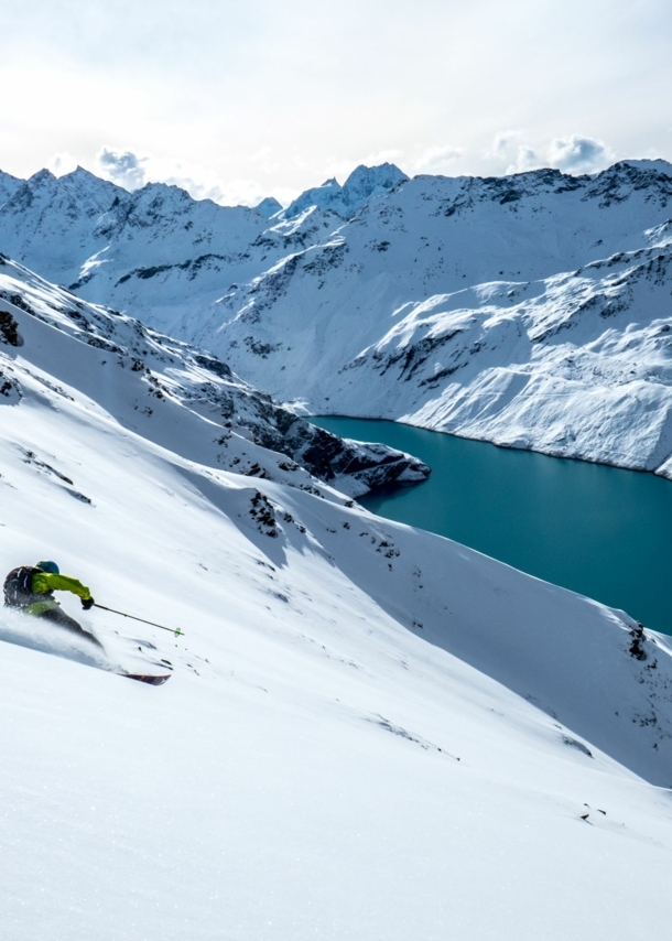 Eine Person auf Ski fährt eine Piste hinunter, im Hintergrund eine Bergkulisse.