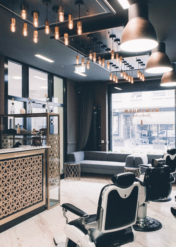 Das Interieur eines modernen Barbershops mit einem Messing verkleideten Tresen, Friseurstühlen aus Leder und einem dunkel gehaltenen cleanen Ambiente