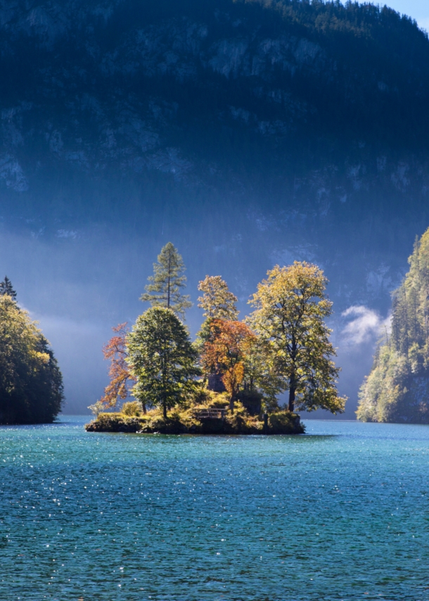 Ein großer See mit einer Insel mit herbstlichen Laubbäumen, eingebettet von riesigen Felswänden