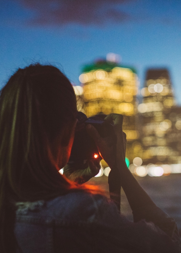 Eine Frau fotografiert in der Dämmerung eine beleuchtete Häuserzeile