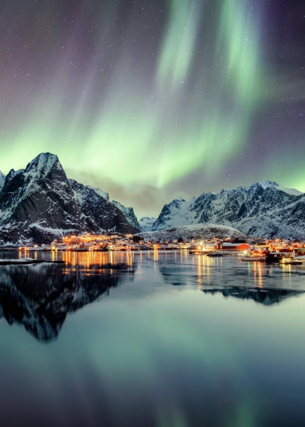 Schneebedeckte Berge und Wasser, darüber grün leuchtende Polarlichter