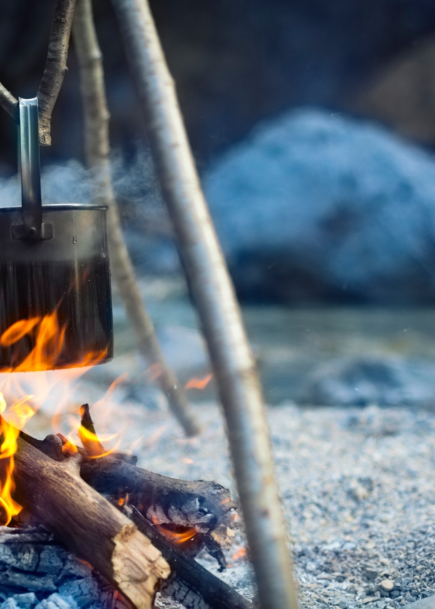 Ein Metalltopf hängt über einer Feuerstelle an einem See in der Dämmerung