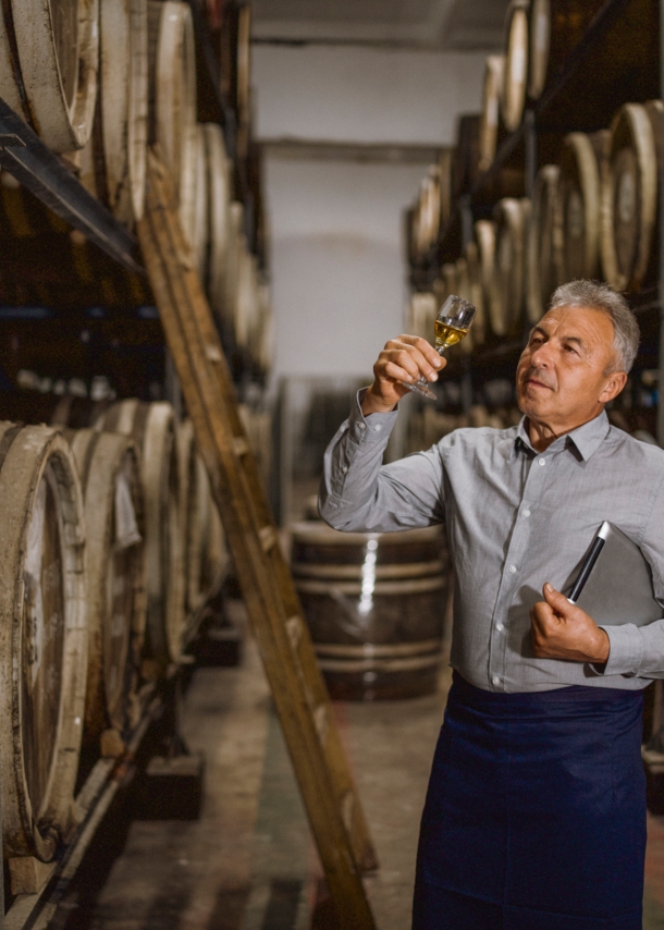 Ein Brandmeister steht in seiner Destillerie und hält ein Glas seines Whiskys prüfend gegen das Licht