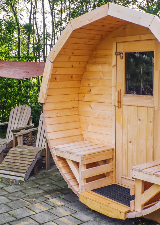 Fasssauna aus Holz im Garten mit Liegestühlen