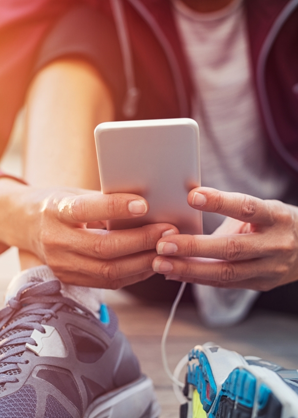 Sportlich gekleidete Person sitzt auf dem Boden und hält ein Handy in der Hand.