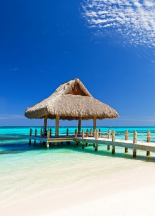 Ein weißer Sandstrand mit Steg und Pavillon am türkisfarbenen Meer in der Dom Rep