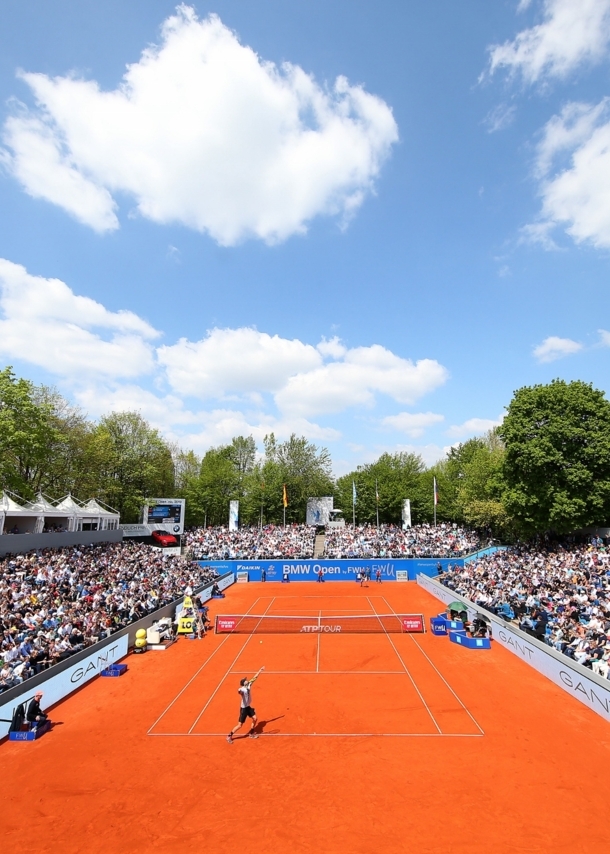 Tennisspieler spielen auf einem Sandplatz, umgeben von zahlreichen Zuschauern.