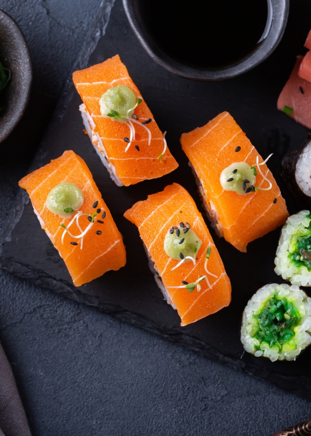 Veganes Sushi auf einer Schieferplatte angerichtet mit Sojasoße und Algensalat