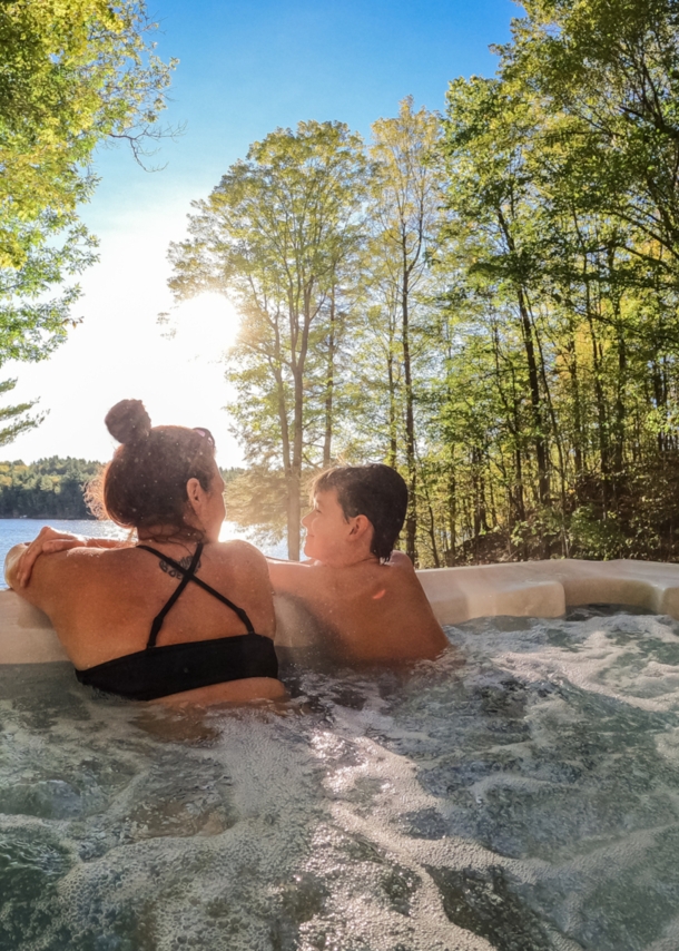 Mutter und Sohn entspannen im Outdoor-Whirlpool und blicken dabei auf einen See