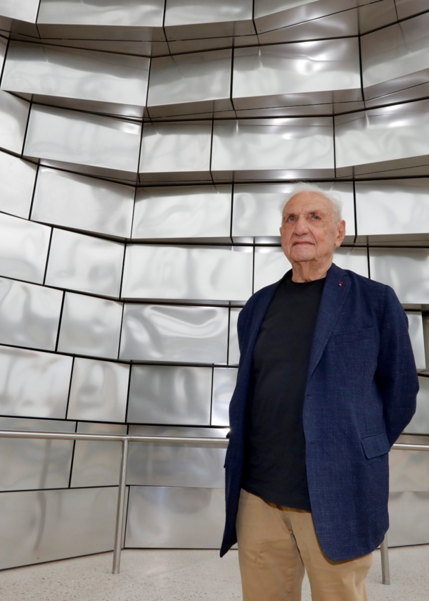 Architekt Frank Gehry vor einer Fassade aus glänzenden Aluminiumplatten