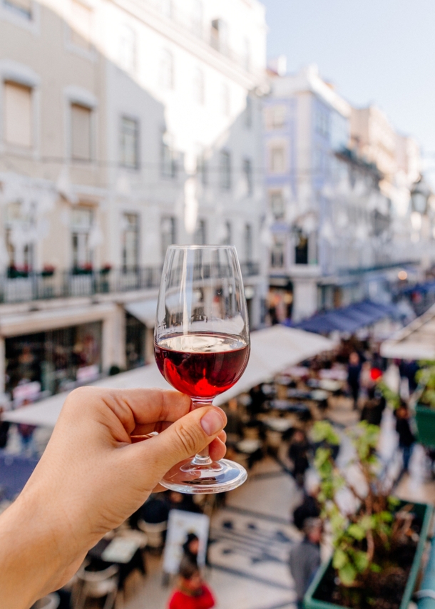 Eine Hand hält ein Glas Portwein oberhalb einer belebten Gasse in die Luft