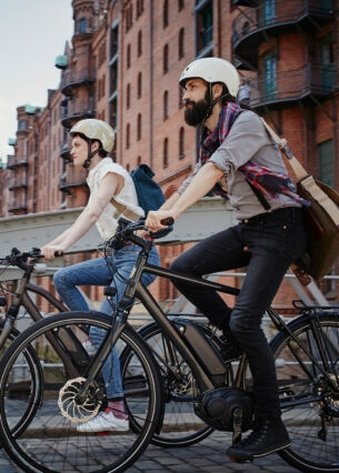 Ein Mann und eine Frau mit Fahrradhelmen fahren auf E-Bikes durch die Hamburger Speicherstadt.