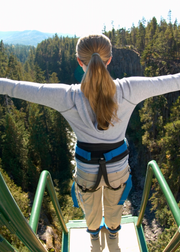 Eine Frau steht mit ausgebreiteten Armen gesichert an einem Bungee-Jumping-Gerüst und ist kurz davor runterzuspringen