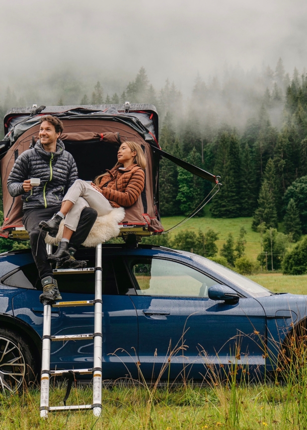 Eine Frau und ein Mann an einem Auto mit Dachzelt