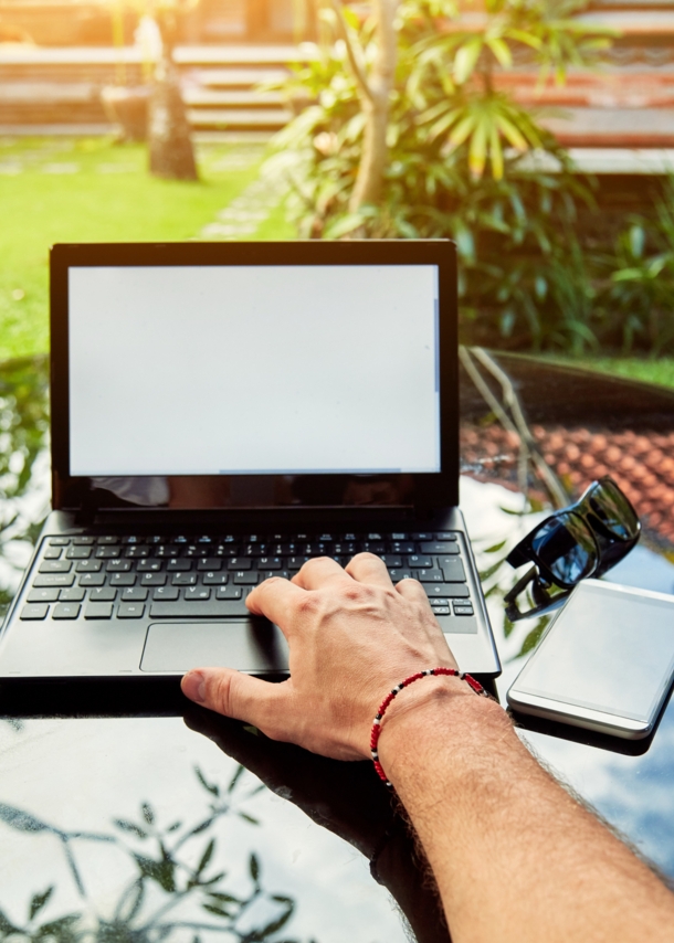 Blick auf einen Laptop, der auf einem Tisch in einem tropischen Garten steht.