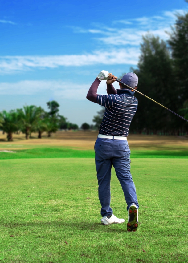 Ein Golfspieler von hinten auf einem Golfplatz, im Hintergrund Palmen