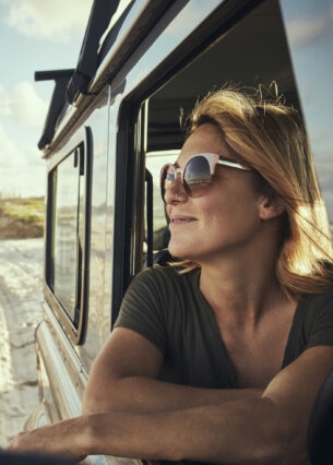 Eine lächelnde Frau mit Sonnenbrille in einem Auto am Strand