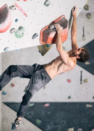 Ein durchtrainierter Mann an einer Kletterwand in einer Boulderhalle