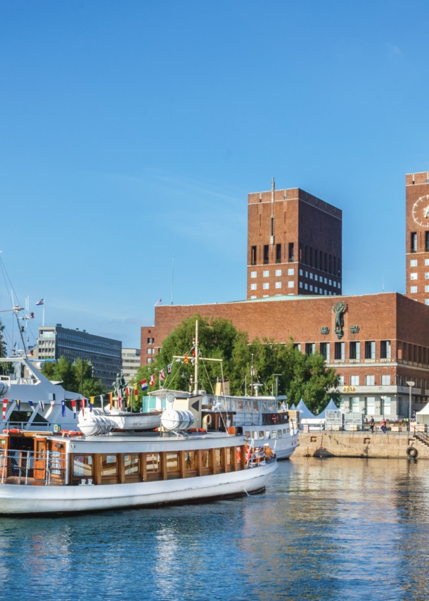 Blick auf das rote Rathaus von Oslo mit Backsteintürmen vom Wasser aus, im Vordergrund Segelboote