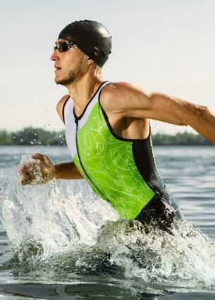 Ein durchtrainierter Triathlet mit Badekappe und Schwimmbrille rennt ins Wasser