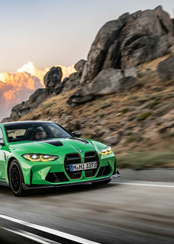 Ein grüner BMW auf einer Landstraße, im Hintergrund große Wolken und Berge