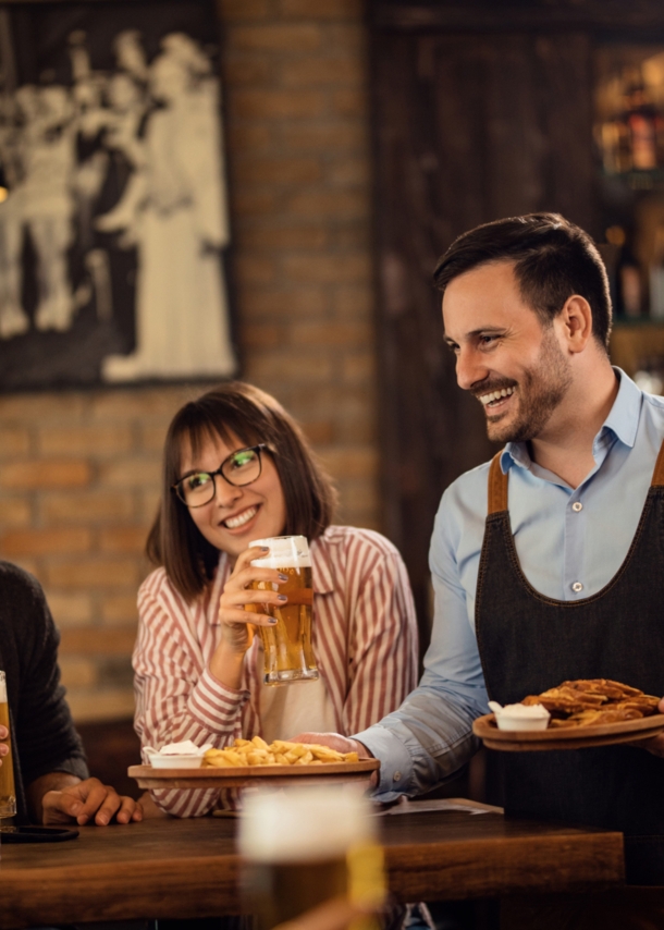 Lächelnder Kellner, der einer Gruppe von Gästen in einem Pub Essen bringt