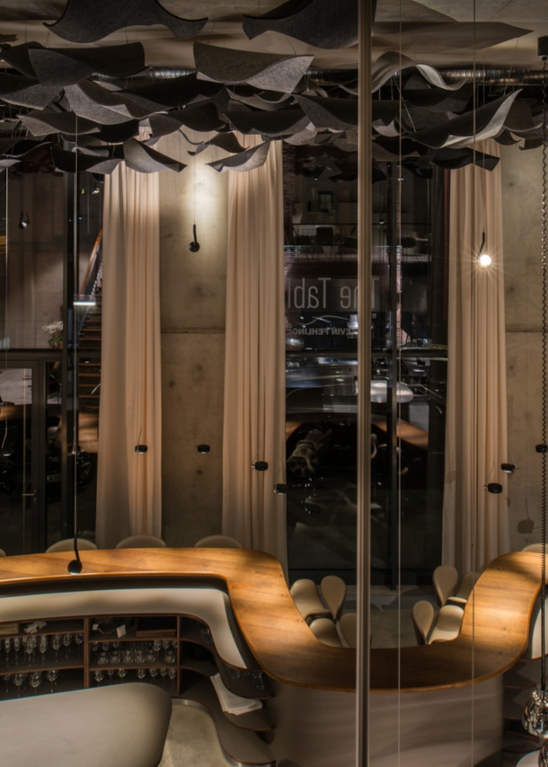 Blick auf das leere Restaurant The Table mit dem geschwungenen Holztisch und hohen Fenstern im Hintergrund