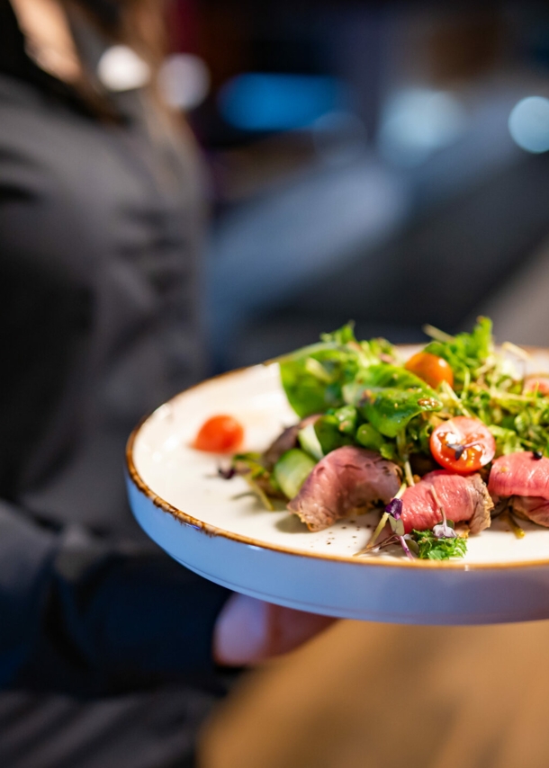 Eine Person hält einhändig einen Teller, auf dem ein Salat angerichtet ist.