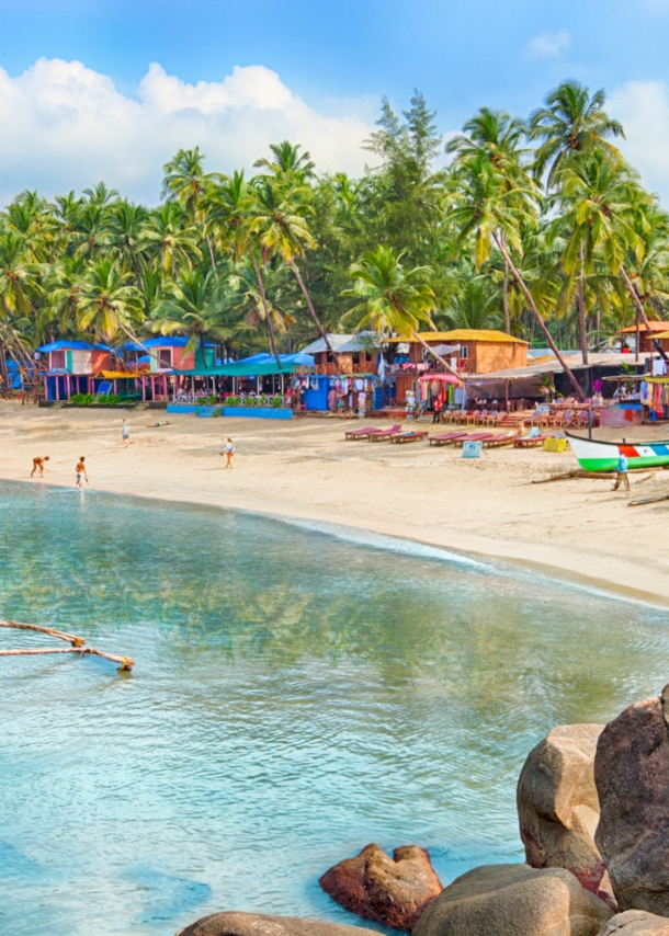 Strand mit bunten Holzhütten und Palmen, im Vordergrund Felsen