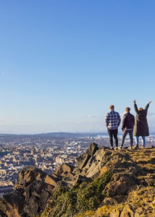 Drei Personen stehen auf einer Erhöhung und blicken von dort über Edinburgh