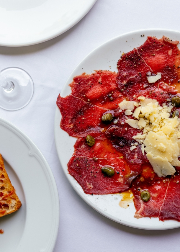 Weiße Teller mit geröstetem Brot und Carpaccio und ein Sektglas