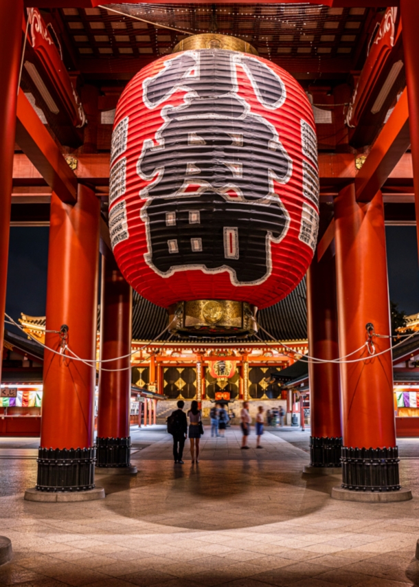 Rote Säulen und überdimensionale Laternen mit japanischen Schriftzügen in einem Tempel