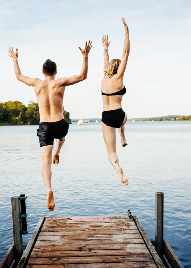 Rückansicht eines Paares in Badekleidung, das von einem Steg in einen See springt