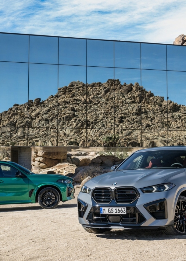 Ein silberner und ein grüner BMW-SUV in einer Landschaft aus Stein und Sand