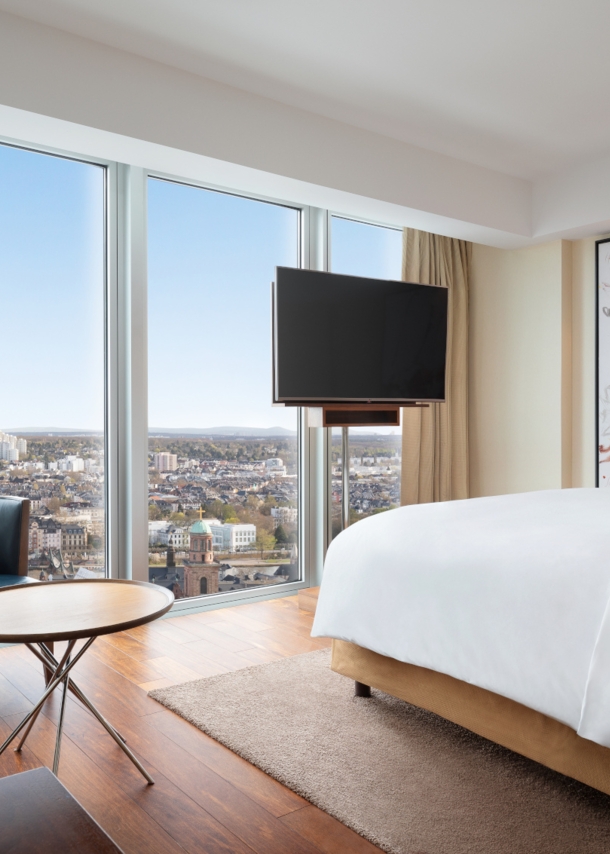 Eine moderne, helle Hotelsuite mit bodentiefen Fenstern und Panoramablick auf Frankfurt am Main