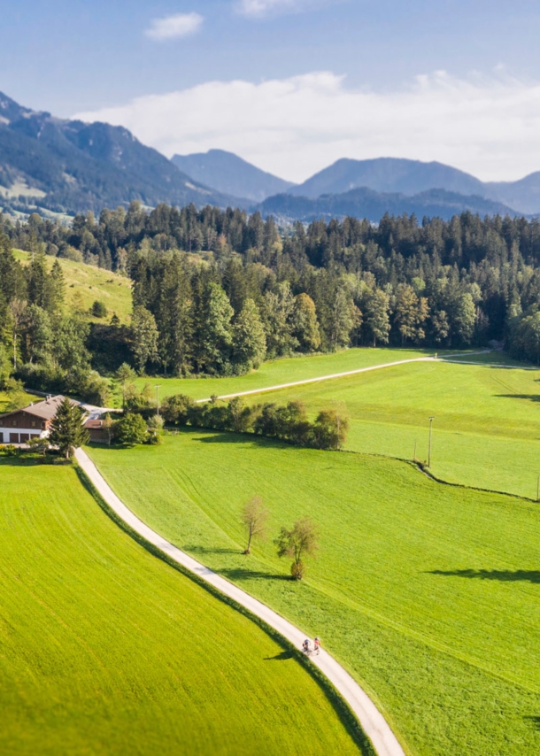 Blick auf eine Landschaft mit Bergen, Wiesen und einem Bach