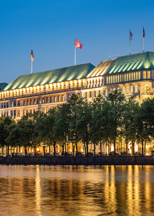 Beleuchtete Außenfassade des Hotels Vier Jahreszeiten am Wasser in der Dunkelheit.